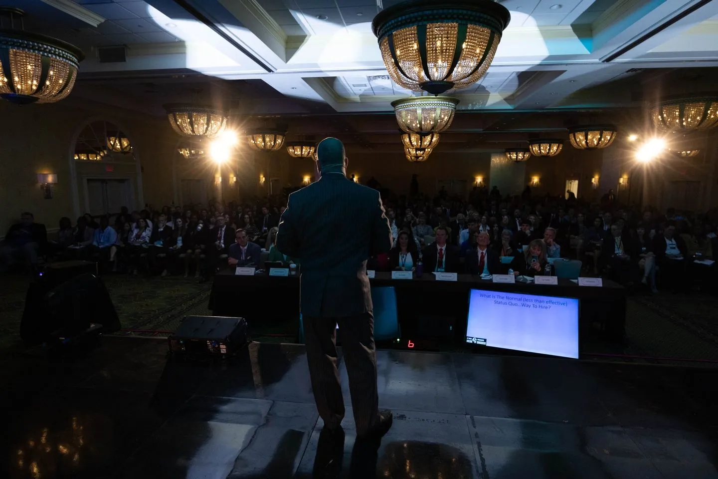 Craig T. Ingram on stage, seen from behind, facing a full ballroom audience